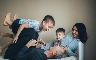 Ein Elternpaar mit zwei kleinen Kindern tobt auf einem Bett.