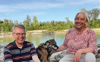 Pfarrersehepaar Rother sitzt mit Hund am See