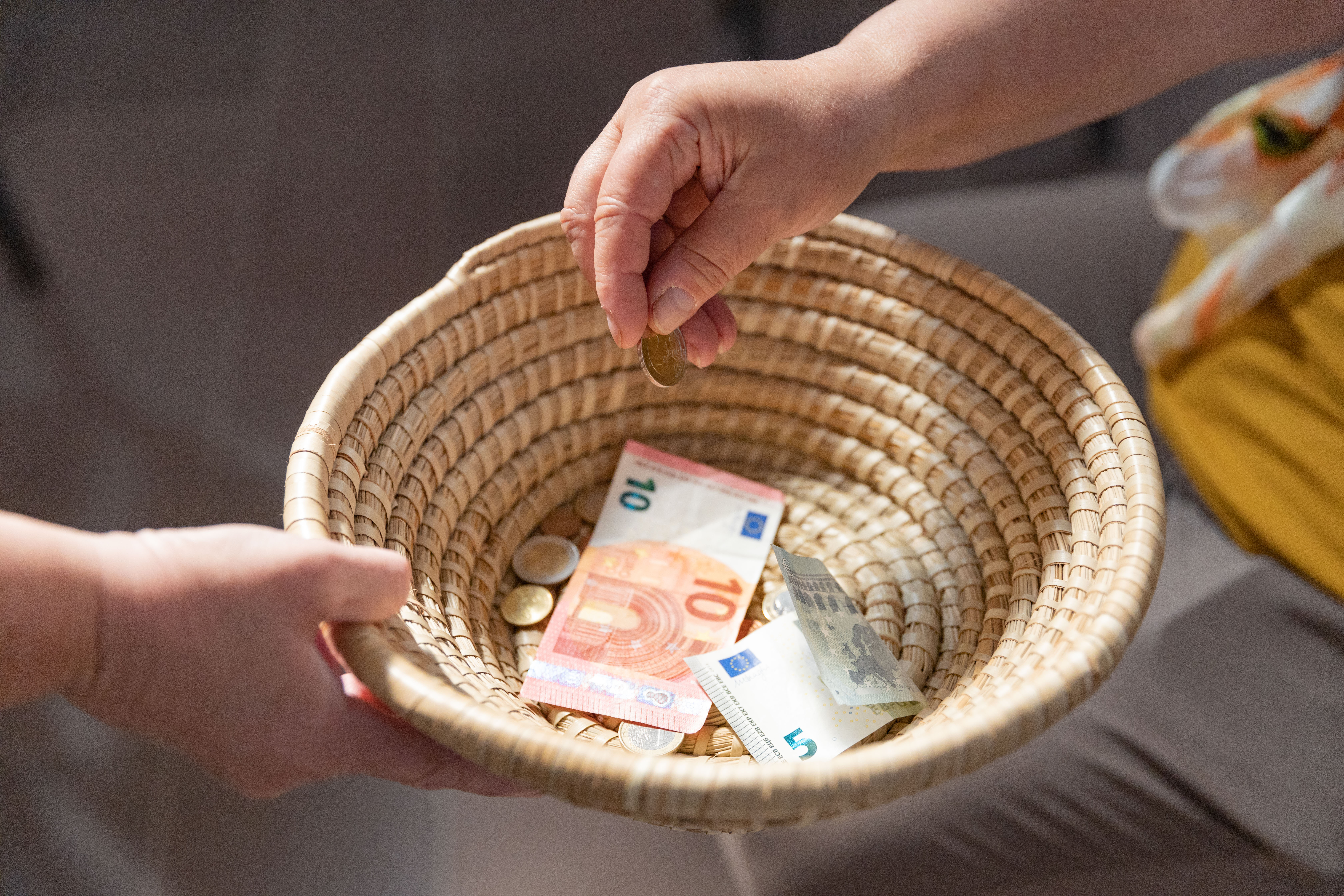 Ein geflochtenes Körbchen wird herumgereicht, um Geld einzusammeln. Ein paar Scheine und Münzen befinden sich bereits darin